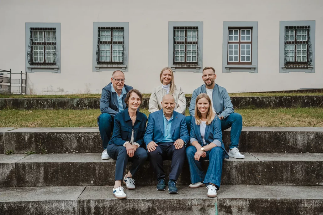 Das Fördermittelberater-Team der Deutschen Fördermittelberatung sitzt gemeinsam auf Steinstufen vor einem Gebäude. Die Personen wirken offen, vertrauenswürdig und engagiert. Ihr Handeln in der Fördermittelberatung ist von Verantwortung, Fachkompetenz und gegenseitigem Vertrauen geprägt.